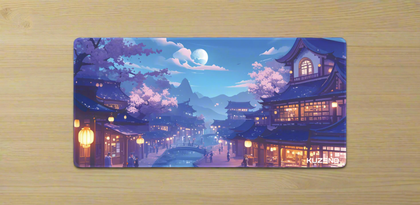 Lantern Glow Kuzeno Gaming Mousepad displayed on a wooden desk, featuring a serene Japanese village at night, illuminated by glowing lanterns and surrounded by cherry blossoms.
