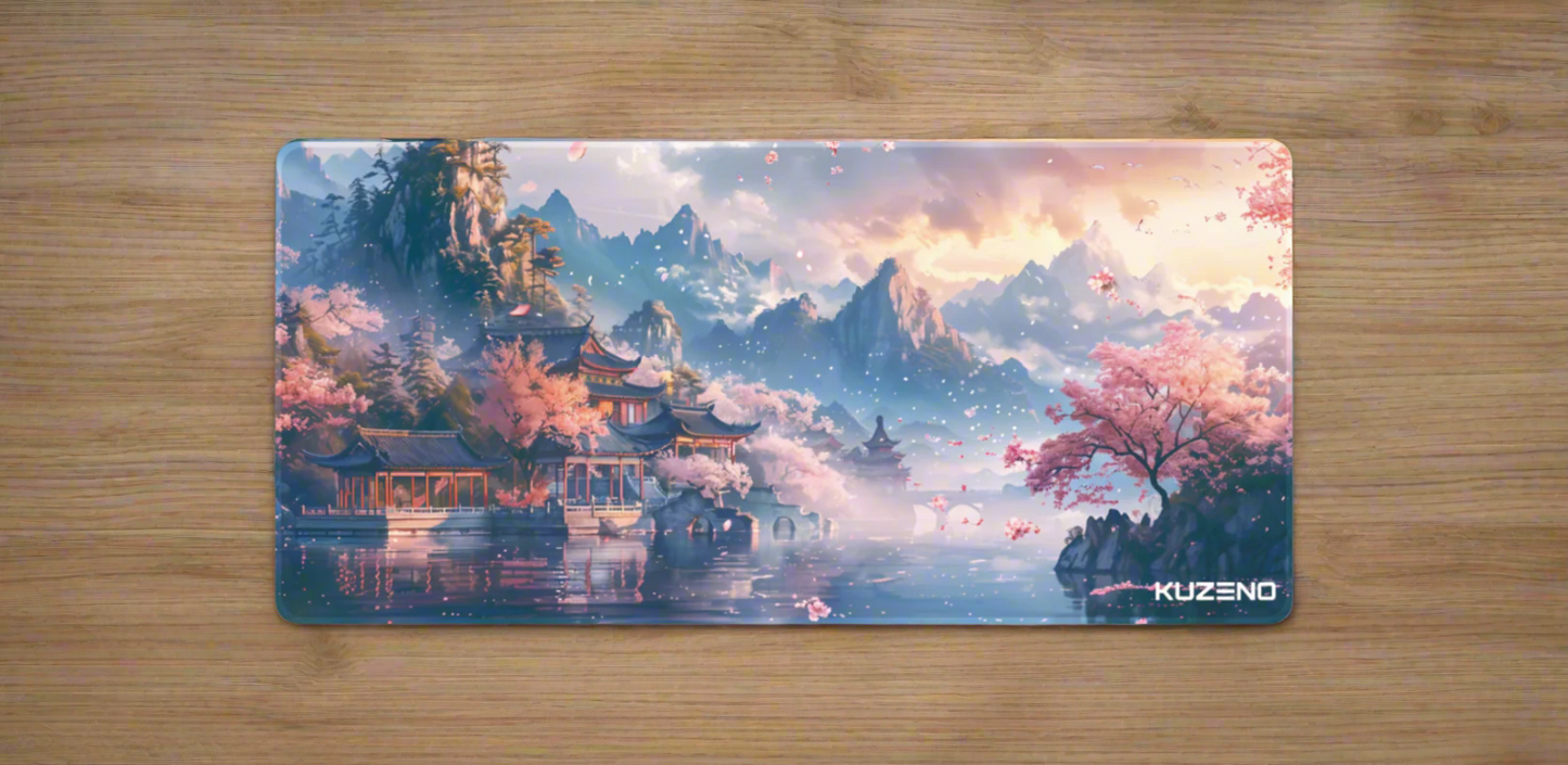 Petal Paradise Kuzeno Gaming Mousepad displayed on a wooden desk, featuring a tranquil landscape with cherry blossoms, a pagoda, and majestic mountains.