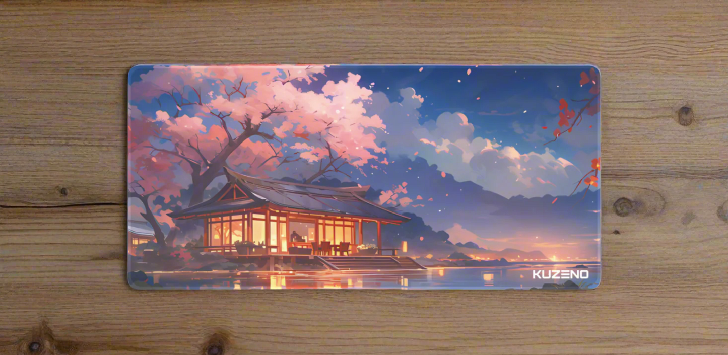 Twilight Haven Kuzeno Gaming Mousepad displayed on a wooden desk, featuring a serene twilight scene with a softly lit Japanese house and blooming cherry blossoms.